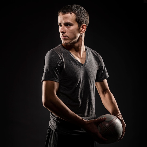 Photo side view of handsome male rugby player holding ball