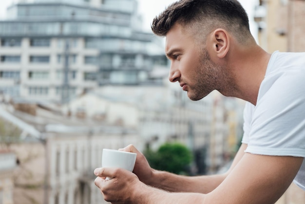 バルコニーでコーヒー カップを保持しているハンサムな男の側面図