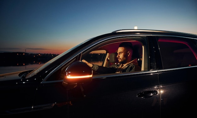 Side view of handsome unshaved man in fashionable clothes that riding his automobile