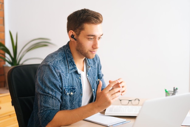 Side view of handsome young business man in earphone having\
online video conference on laptop at home office