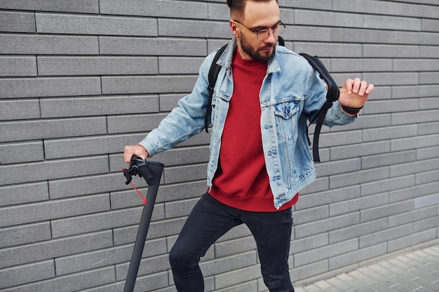 Side view of handsome young guy in casual clothes that riding electric schooter outdoors at sunny daytime