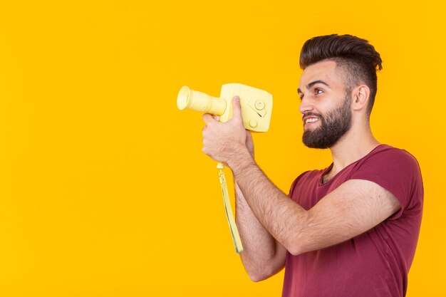 Vista laterale di un bel giovane maschio hipster con la barba spara oggetti su una videocamera vintage