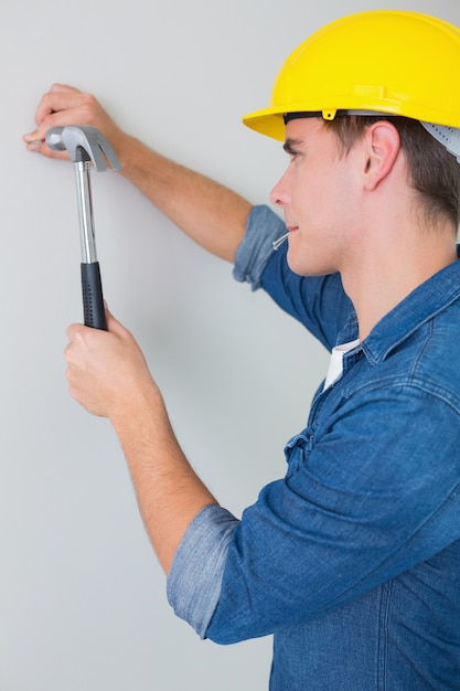 Side view of handyman hammering nail in wall