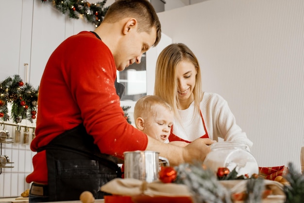 Вид сбоку на счастливую забавную семью, мать, отец и маленький сын пекут рождественское печенье на уютной кухне дома