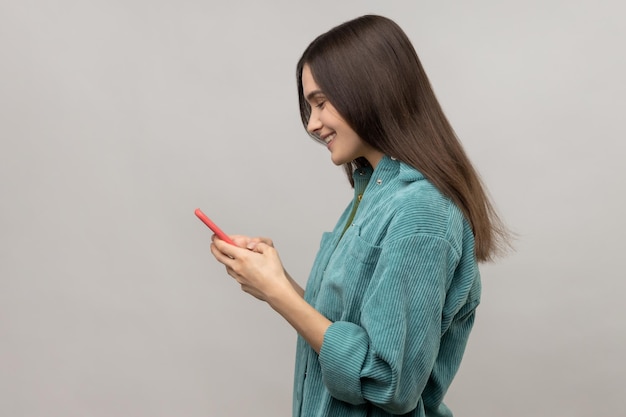 Side view of happy woman reading message on smartphone and smiling using mobile device