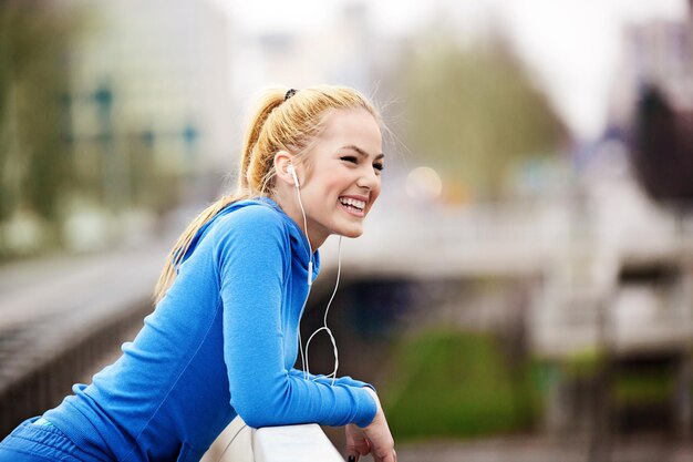 Side view of happy young woman listening music while relaxing on bridge