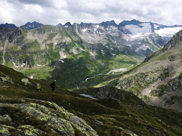 Side view of hiker standing on mountain against cloudy sky