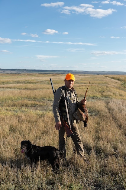 Side view of hunter carrying dead pheasant while walking on field