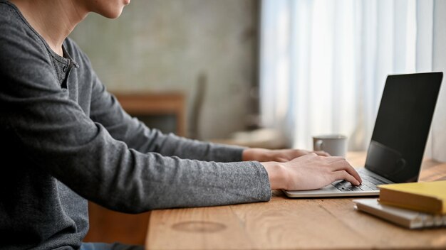 Vista laterale dell'immagine di un giovane asiatico che digita sulla tastiera utilizzando il computer portatile che lavora in remoto al bar