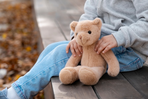 Photo side view kid holding teddy bear outdoors