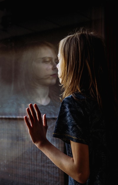 Photo side view of a kid standing against the window