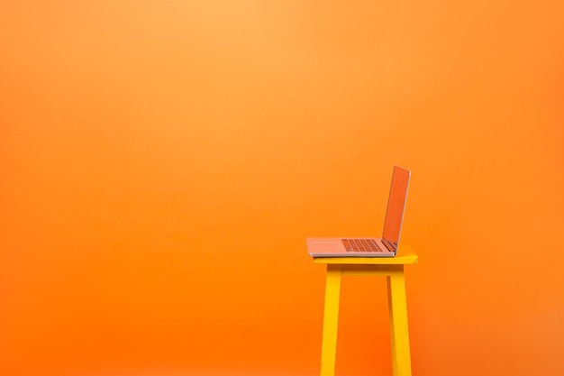 Side view of laptop on chair and empty copy space on the left side for advertising, wireless connection free wifi, freelance job and or business in internet. orange background, indoor studio shot