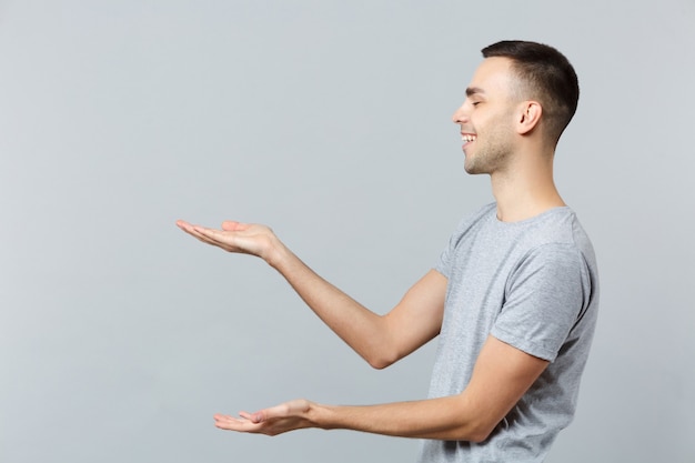 Foto vista laterale del giovane ridente in abiti casual che punta le mani da parte, tenendo qualcosa