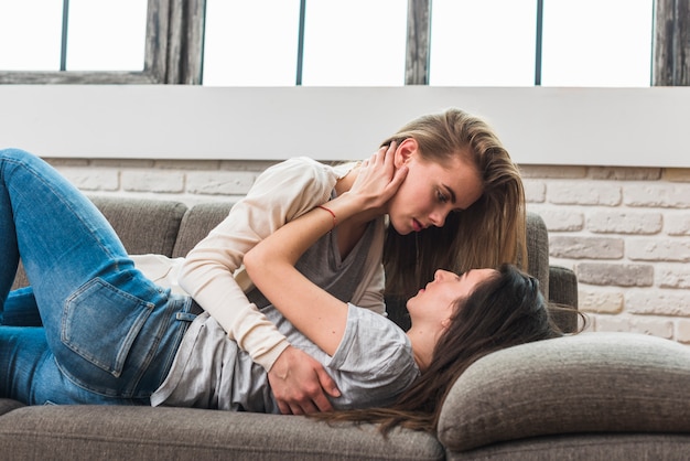 Photo side view of lesbian young couple lying on grey sofa looking at each other