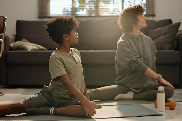 Photo side view of little boy doing stretching exercise with his mother