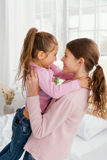 Photo side view of little sisters together at home