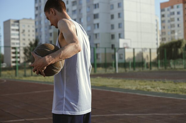 Side view of male basketball player with ball standing on streetball court in summer