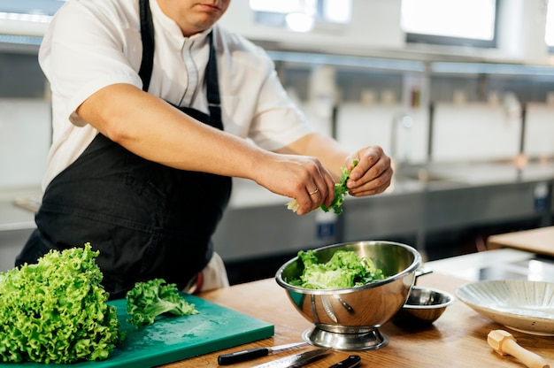 Photo side view of male chef tearing salad in bowl