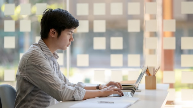 Side view of male entrepreneurs typing on laptop computer in glass wall office