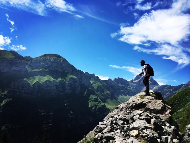 Side view of male hiker standing on mountain against blue sky during sunny day