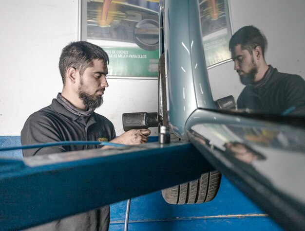 Side view of male master using electric screwdriver while fixing wheel of automobile