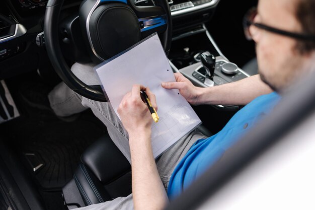 Foto vista laterale sul documento di riempimento meccanico maschio durante l'ispezione dell'auto l'uomo si siede all'interno dell'auto e guarda la carta
