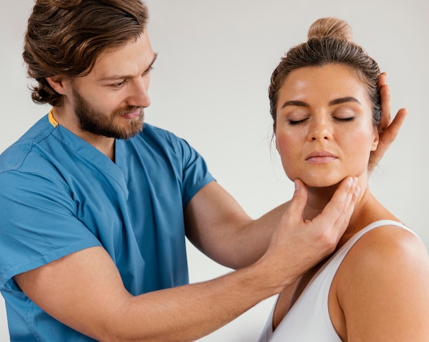 Vista laterale del terapista osteopatico maschio che controlla il collo del paziente femminile