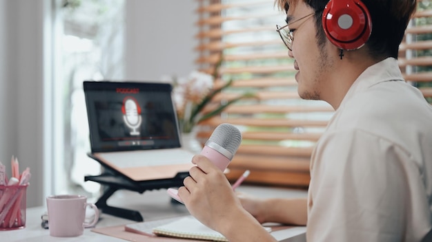 Side view of male using laptop and microphone recording podcast\
from home studio recording podcast from home studio radio podcasts\
blogging concept