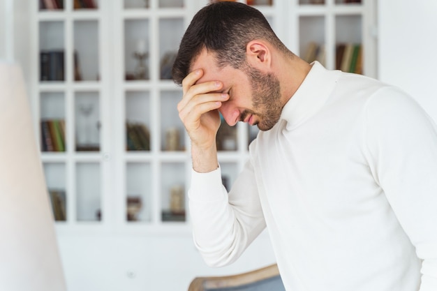 目を閉じて額に手で触れている男性の側面図