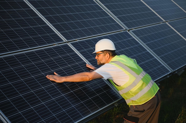 Вид сбоку на рабочего-мужчину, устанавливающего солнечные модули и опорные конструкции фотоэлектрической солнечной батареи. Электрик в защитном шлеме во время работы с солнечной панелью. Концепция солнечной энергии