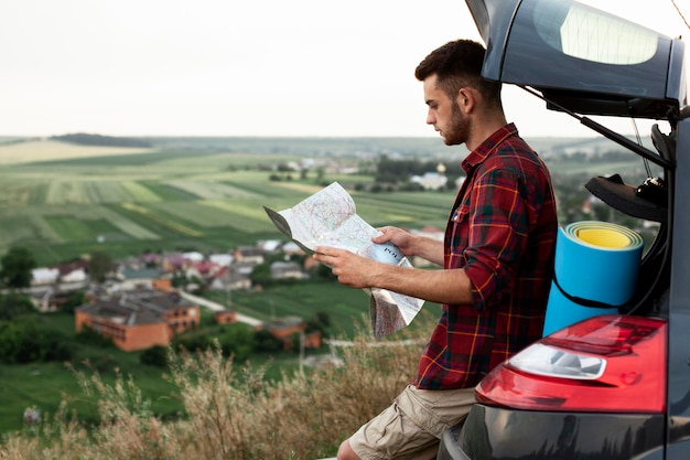 Foto uomo di vista laterale nella mappa della lettura dell'automobile