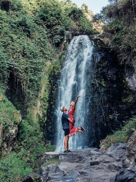 side view of man carrying woman while standing against waterfall