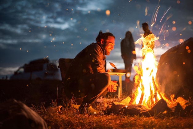 Photo side view of man crouching by campfire at night