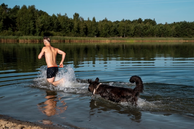 Foto uomo e cane di vista laterale che corrono in acqua