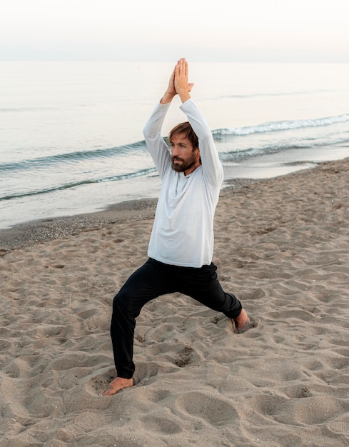 Vista laterale dell'uomo che fa yoga sulla spiaggia