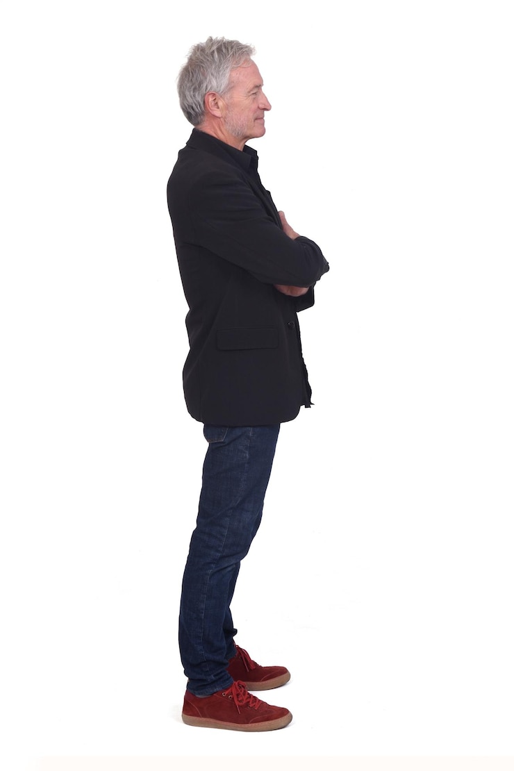 Side view of man dressed in jeans sneakers and blazer with arms crossed on white background