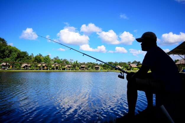 Side view of man fishing in lake against blue sky