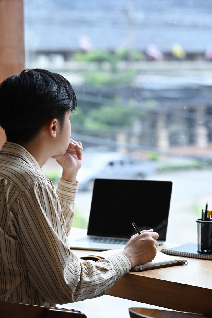 Photo 측면 보기 남자 프리랜서는 창 근처에 앉아서 노트북 컴퓨터로 작업합니다.