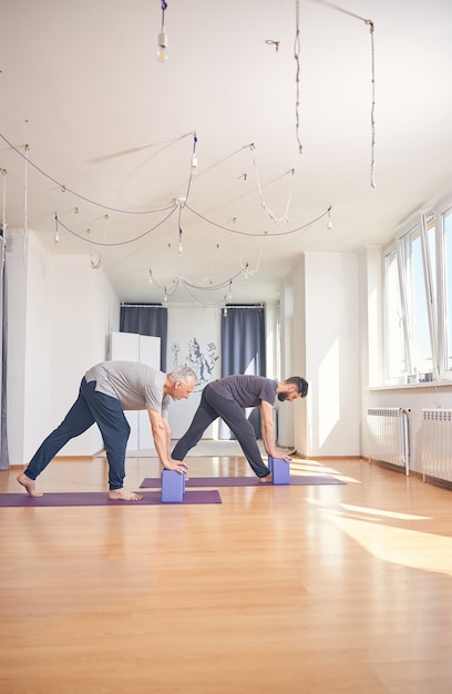 Side view of a man and his personal trainer doing a forward bend supported with foam blocks