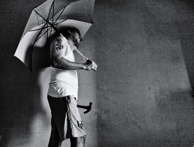 Foto vista laterale di un uomo con un ombrello in piedi vicino al muro