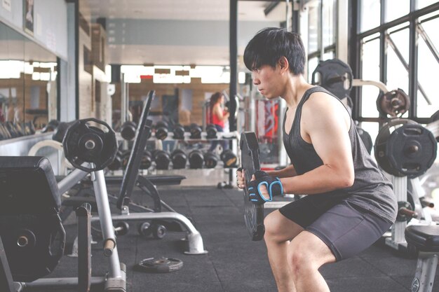 Side view of man holding weights while sitting in gym