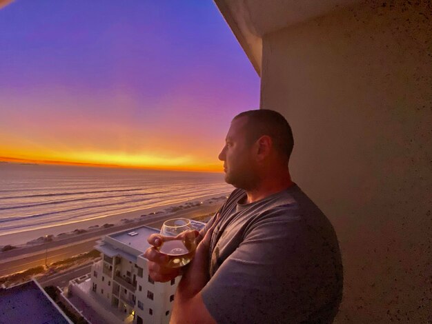 Side view of man looking away while standing against sky during sunset