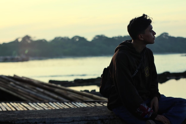 Photo side view of man looking at lake against sky during sunset