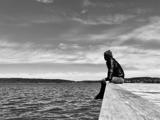 空に向かって埠頭に座っている男が湖を見ている側面の景色