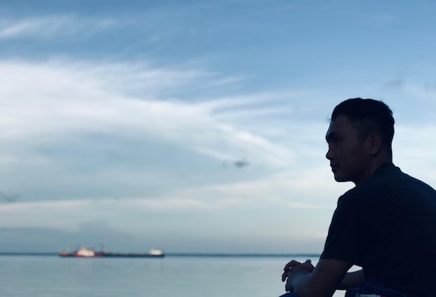 Photo side view of man looking at sea against sky during sunset