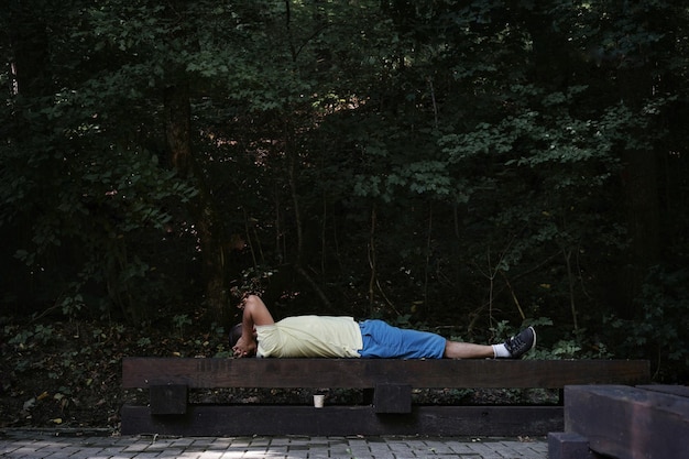 Foto vista laterale di un uomo sdraiato su una panchina contro le piante