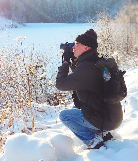 side view of man photographing on snow covered field
