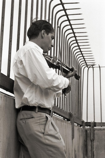 Foto vista laterale di un uomo che suona il violino vicino alla ringhiera