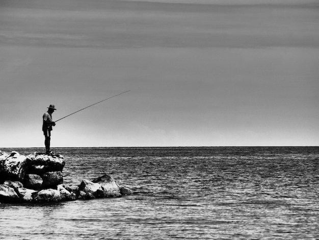 Photo side view of man on rocks fishing in sea