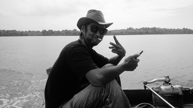 Photo side view of man showing peace sign in boat on lake